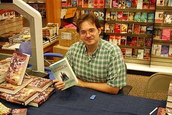 Photo of Brandon Sanderson at a book signing holding a copy of his book Elantris