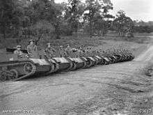 A row of open topped armoured vehicles lined up across a dirt row with their crews