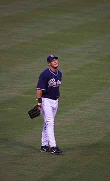 A baseball player wearing a white uniform standing in the field.