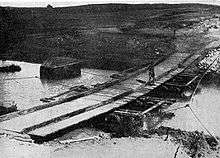 The bridge was constructed by the New Zealand Mounted Rifles Brigade. Long planks of wood were laid across the stream on empty wine casks; shorter planks were then laid on top crosswise to form a flat surface.