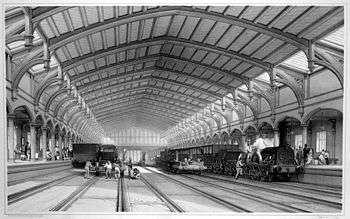 Two trains and two empty rail tracks below an ornate roof which recedes into the distance