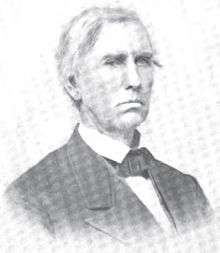 A man with gray hair wearing a black jacket and tie and white shirt