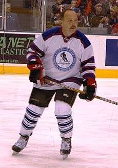 "A colour photo of Bryan John Trottier while skating with no helmet in a hockey rink in uniform. "