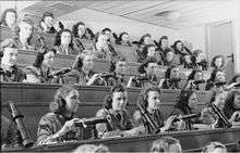 A group of young women, wearing headsets, sitting in an auditorium, controlling projectors.