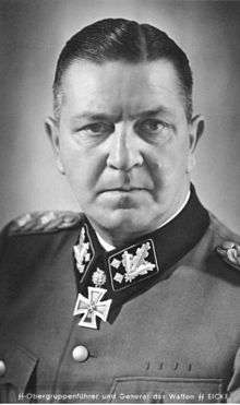 A black-and-white photograph of a man in semi profile wearing a military uniform and neck order, in shape of an Iron Cross. His dark hair is combed to the back. He has determined facial expression.