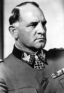 A black and white photograph of a man in semi profile wearing a military uniform and neck order, in shape of an Iron Cross. He has short, thinning hair and a determined facial expression.