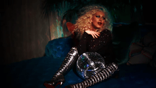 A picture of a blond woman looking to her left with a disco ball between her legs