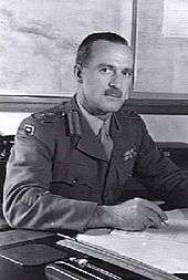 Head-and-shoulders portrait of moustachioed man in military uniform at desk