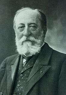 bust-length portrait of Saint-Saëns with a beard in a vest and suit, looking at the viewer