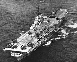 A black and white photo of a large aircraft carrier with aircraft filling its deck.