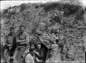 A black and white photograph of a group of men in military uniform in a trench in front of a sign which reads: The Cannibals Paradise Supply Den Beware