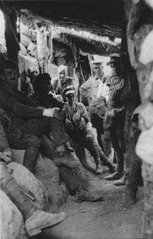 Soldiers sitting and standing in a trench covered by logs