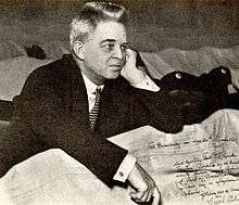 photograph of Carl Nielsen in a dark suit and tie sitting behind crumpled papers including a letter with his signature