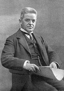 Carl Nielsen, seated, facing right, smartly dressed in a suit and waistcoat