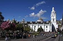 A square with a large white church with one tower and several cuppolas.