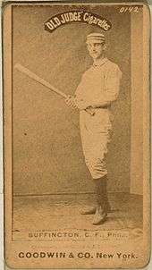 A baseball player is standing, facing the camera, holding a baseball bat.