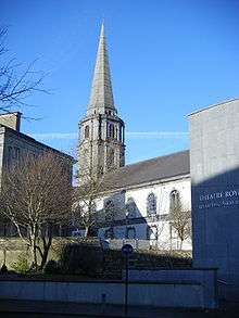 A Large Church spire can be seen above and behind a theatre and a deciduous tree with leaves shed.