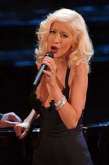 A blonde woman holding a microphone wearing a black dress.