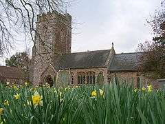 Stone building with prominent square tower. In the foreground are daffodils.