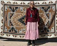 Clara Sherman standing in front of her woven Navajo rug