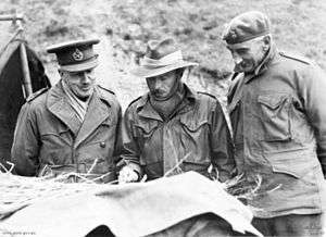 Three men study a map. They are wearing military uniforms, with a peaked cap, a slouch hat and a beret, but are dressed warmly  against the cold with scarves and gloves.