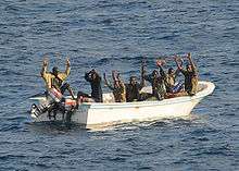 Seven men in a small motor skiff with their hands raised.