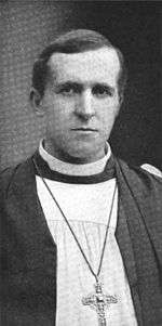 A young-looking dark-haired man faces forward. He is wearing black and white robes and a crucifix.