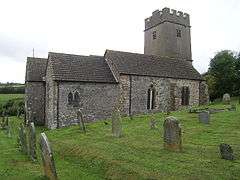 Stone building with square tower. In the foreground are gravestones.