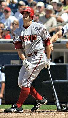 A man in red socks and a gray baseball uniform with "Arizona" on the chest stands after taking a right-handed baseball swing.