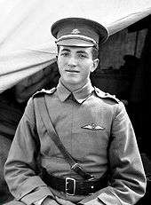 Half-length outdoor portrait of young man in military uniform and peaked cap, with pilot's wings on left breast pocket