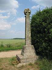 A stone post, topped with a cross, stands next to a bush in a field. An inscription on its base reads, "Battle of Towton Palm Sunday 1461".