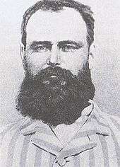 Black and white photograph of the head and shoulders of a bearded man wearing a striped top