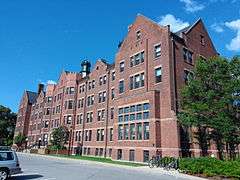 An elongated five-story reddish brown brick dormitory on a clear day