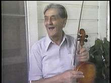 An image of Dennis McGee holding his violin during an interview with PBS's American Patchwork.
