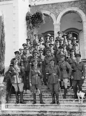 Soldiers in cavalry uniform on steps outdoors, with canine mascot