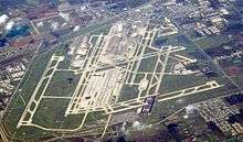 An aerial view of an airport, with long stretches of runway scattered across a large green patch.