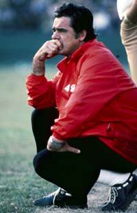 Photo of Nolan wearing a red San Francisco 49ers jacket and black pants crouching on the sideline