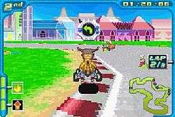An orange bipedal dinosaur rides a small go-kart around the corner of a paved race track. Two other racers are visible around him. Futuristic buildings appear in the daytime background. Stylized features such as time remaining and a small map of the course adorn the edges of the screen.