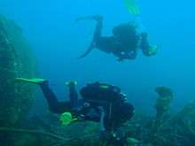 Two divers on a wreck. The one in the background is deploying an inflatable surface marker buoy as preparation for ascent