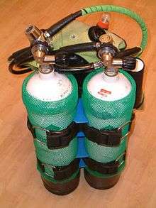 The rear view of a set of twin independent cylinders strapped to a jacket harness, each with a scuba regulator fitted.