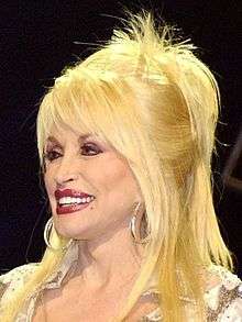 A woman with blond hair wearing large hoop earrings and red lipstick.