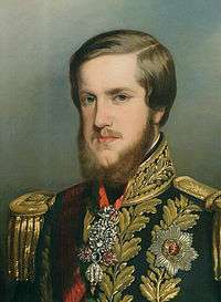 Painted portrait of a young man with auburn hair and a full beard who wears a heavily embroidered military-type tunic bedecked with medals and a sash of office across the chest