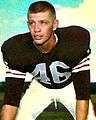 Posed color photo of Don Fleming in three-point stance, wearing brown, black and white uniform of the Cleveland Browns, with helmet off.