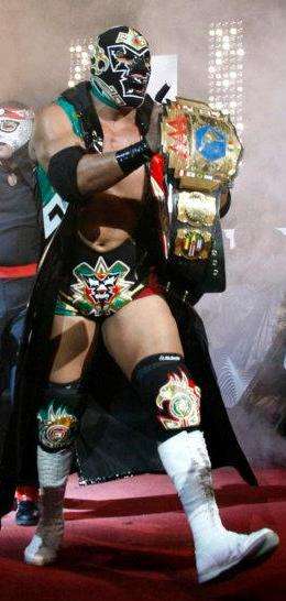 The masked Dr. Wagner Jr. walking to the ring, holding a professional wrestling championship belt in his hands