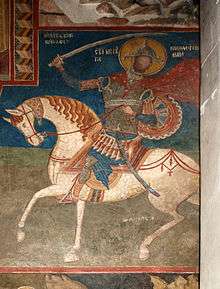 Medieval fresco of an armoured saint on a white horse swinging a sword
