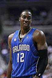 A black basketball player wearing a blue jersey smiles at the camera