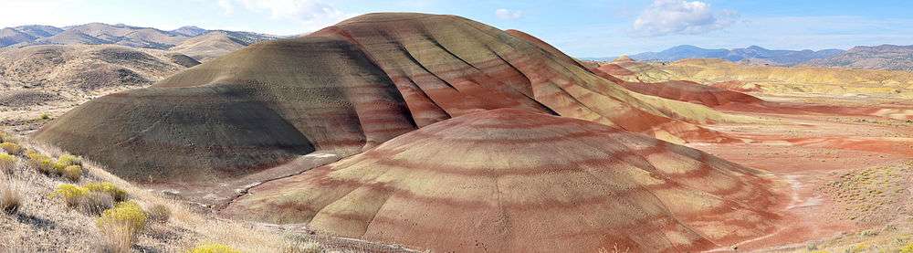 Multicolored rock strata in shades of red and yellow comprise a set of low, bare, rounded hills