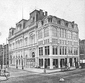 Photograph of the exterior of Booth's Theatre, viewed from diagonally across the intersection of 23rd Street and Sixth Avenue.