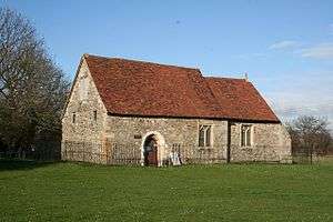 A small, simple stone church with a red tiles roof seen form an angle, with the nave in the foreground and a small chancel beyond