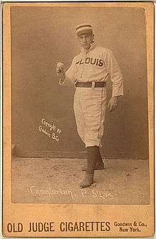 A baseball player is standing, facing the camera, holding a baseball.